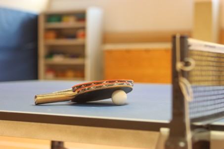 Tischtennisschläger liegen auf einer Tischtennisplatte in einer Sporthalle.